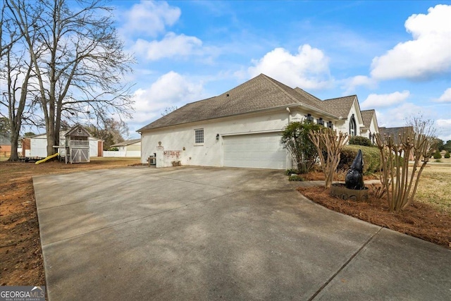 view of side of property with a shingled roof, concrete driveway, an attached garage, and stucco siding