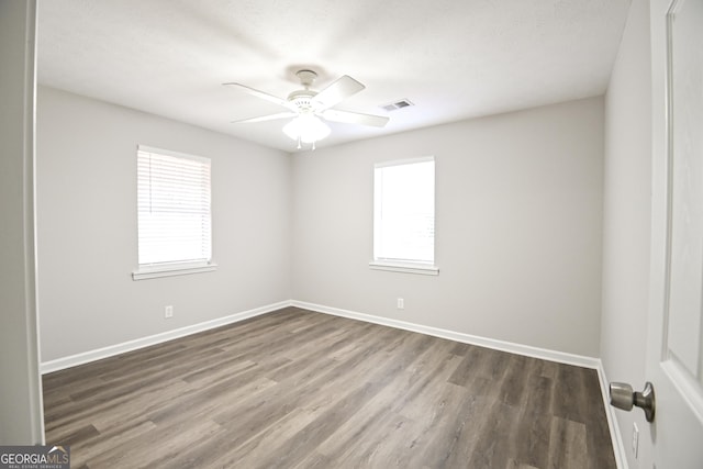 spare room with baseboards, ceiling fan, visible vents, and dark wood-type flooring
