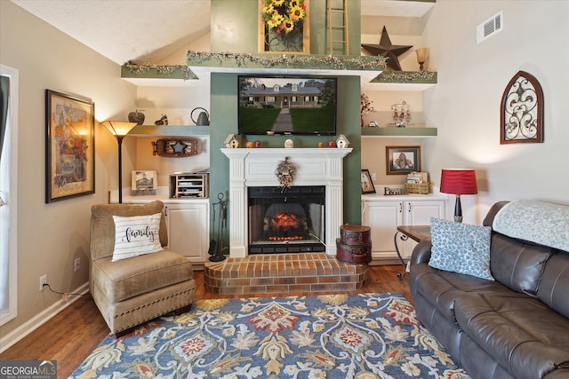 living room featuring built in shelves, visible vents, a lit fireplace, and wood finished floors