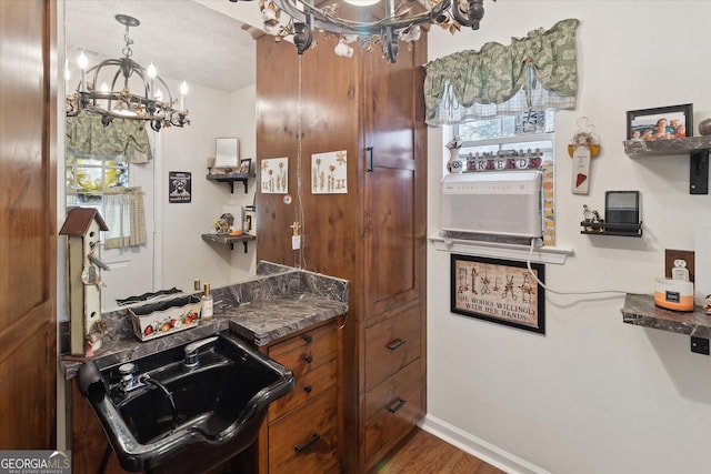 kitchen with a notable chandelier, wood finished floors, baseboards, brown cabinets, and dark countertops