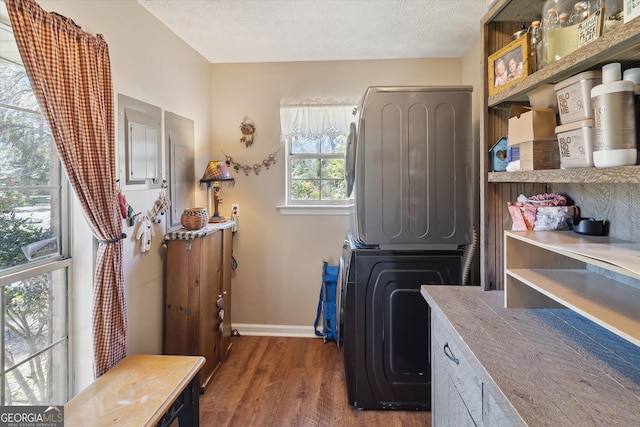 clothes washing area featuring a textured ceiling, laundry area, baseboards, stacked washing maching and dryer, and dark wood-style floors