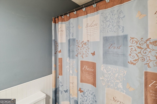 bathroom with a wainscoted wall, a shower with shower curtain, and toilet