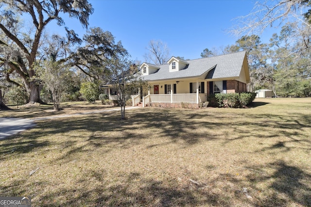 view of front of property with a shingled roof, an outbuilding, covered porch, a storage unit, and a front lawn