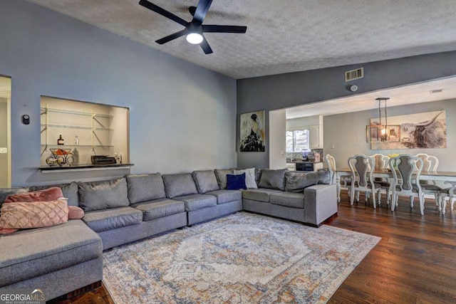 living room featuring a textured ceiling, lofted ceiling, ceiling fan with notable chandelier, dark wood-style flooring, and visible vents