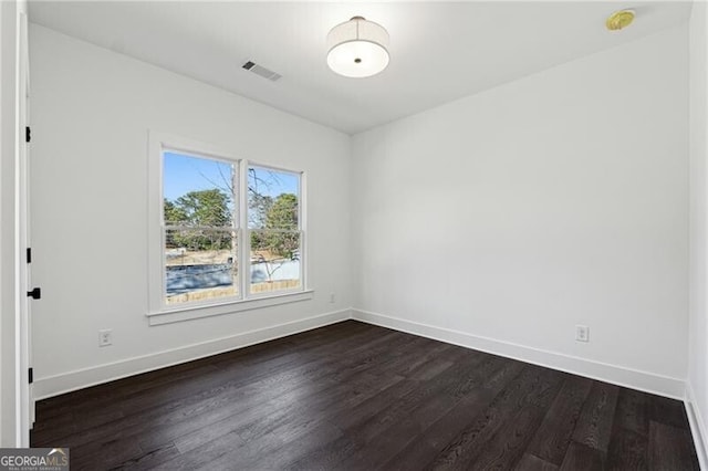 spare room featuring visible vents, dark wood-type flooring, and baseboards