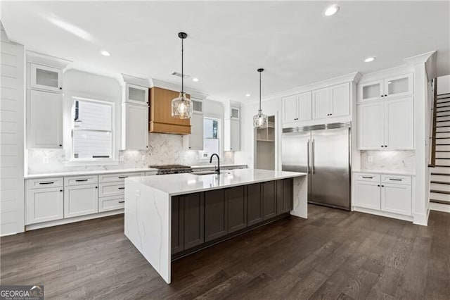 kitchen featuring an island with sink, built in fridge, white cabinets, and light countertops