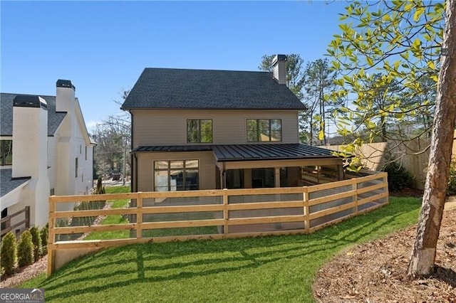 rear view of house featuring a standing seam roof, a chimney, and metal roof