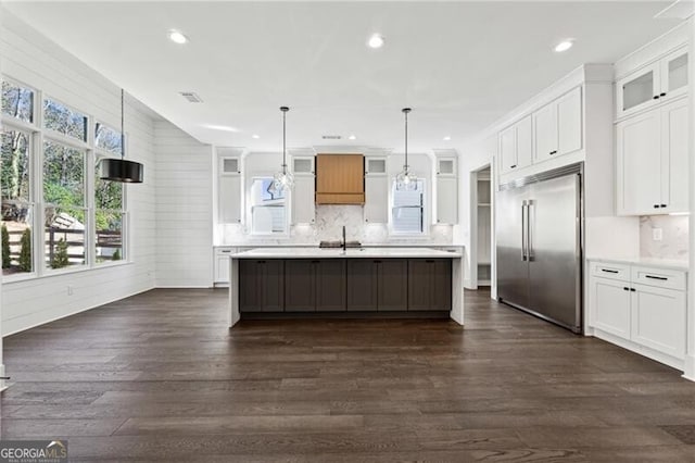 kitchen with stainless steel built in fridge, a sink, dark wood-style floors, light countertops, and glass insert cabinets