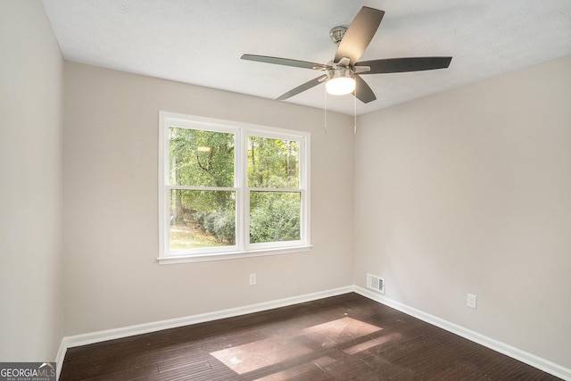 empty room featuring dark wood-style floors, visible vents, and baseboards