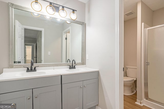 bathroom with a shower stall, toilet, wood finished floors, and a sink