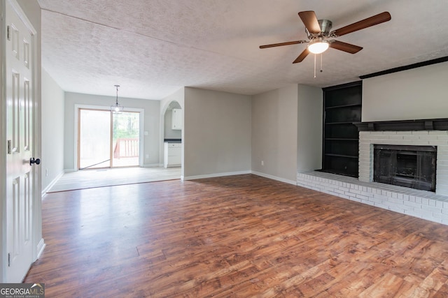 unfurnished living room with built in features, wood finished floors, baseboards, a textured ceiling, and a brick fireplace