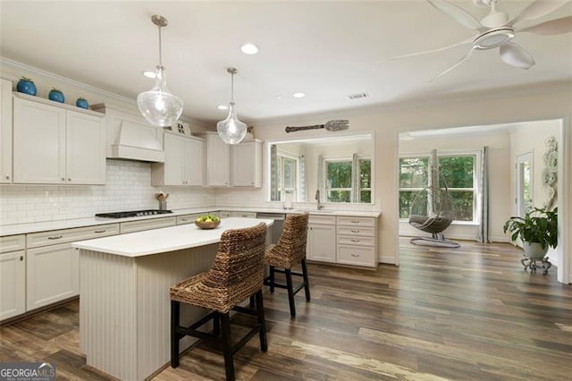 kitchen featuring a kitchen island, ornamental molding, light countertops, custom range hood, and a kitchen bar