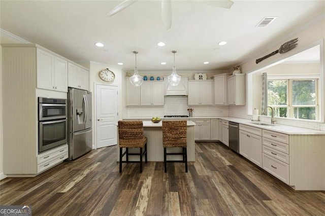 kitchen with a sink, stainless steel appliances, dark wood-type flooring, a kitchen bar, and a center island