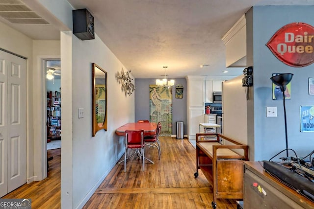 dining area with an inviting chandelier, wood-type flooring, visible vents, and baseboards