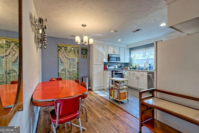 dining space featuring a textured ceiling, recessed lighting, wood finished floors, visible vents, and an inviting chandelier