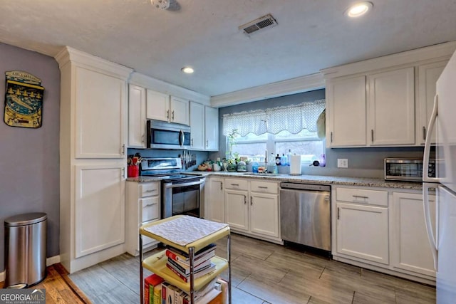 kitchen featuring visible vents, stainless steel appliances, wood finish floors, white cabinetry, and a sink