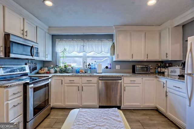 kitchen featuring appliances with stainless steel finishes, wood finish floors, white cabinetry, and a sink