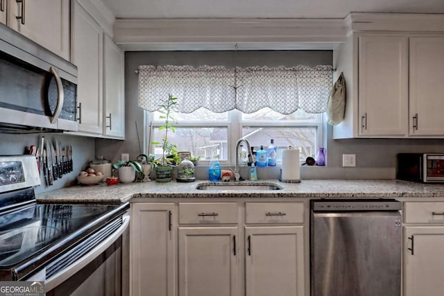 kitchen with light stone countertops, white cabinetry, stainless steel appliances, and a sink