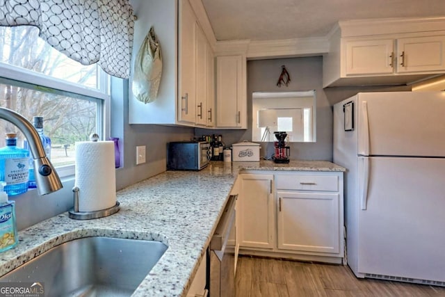 kitchen featuring freestanding refrigerator, a sink, light wood-type flooring, white cabinetry, and stainless steel dishwasher