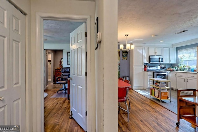 hall featuring a textured ceiling, visible vents, a chandelier, and dark wood-style flooring