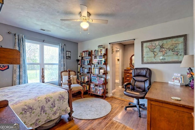 bedroom featuring visible vents, ceiling fan, light wood-style flooring, and a textured ceiling