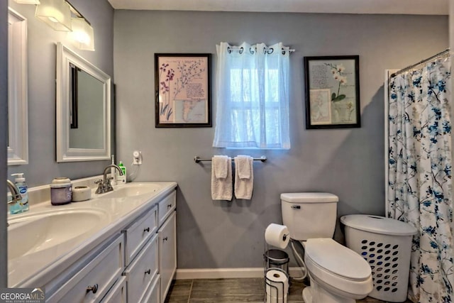 bathroom featuring toilet, double vanity, baseboards, and a sink