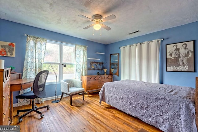 bedroom featuring a textured ceiling, a ceiling fan, visible vents, baseboards, and hardwood / wood-style floors