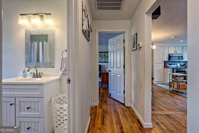 hall featuring dark wood-style floors, baseboards, visible vents, and a sink