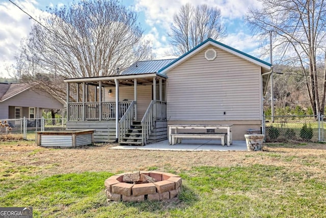 rear view of property featuring an outdoor fire pit, fence, metal roof, and a yard