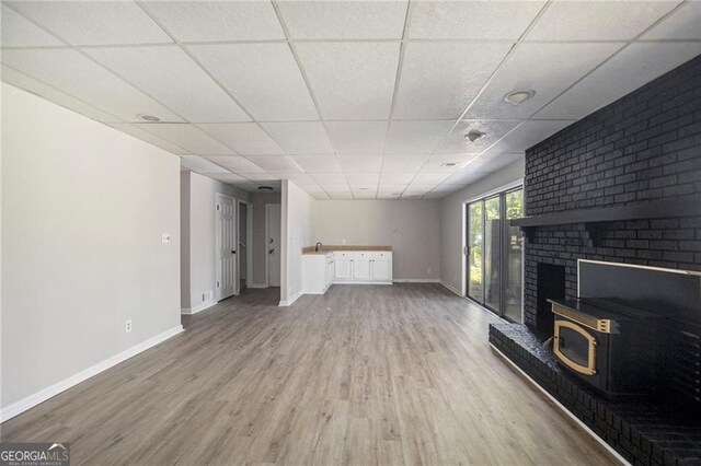 unfurnished living room featuring a paneled ceiling, a sink, baseboards, and wood finished floors