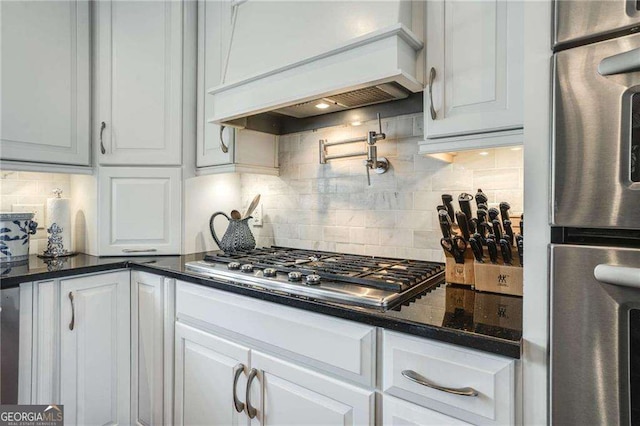 kitchen with white cabinets, decorative backsplash, dark stone countertops, premium range hood, and stainless steel gas cooktop