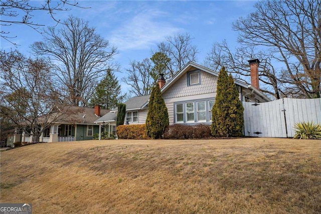 view of front of property featuring a gate, fence, a chimney, and a front lawn