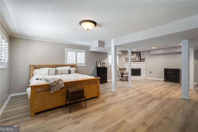 bedroom featuring light wood-style floors, a fireplace, baseboards, and ornate columns