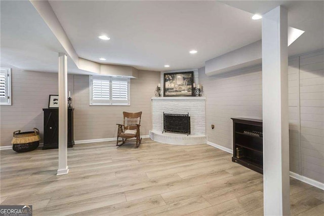 below grade area featuring a fireplace with raised hearth, baseboards, wood finished floors, and recessed lighting