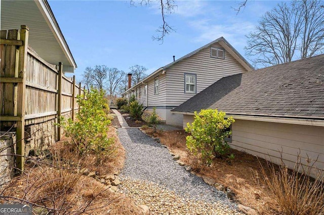 view of side of property with a shingled roof and fence