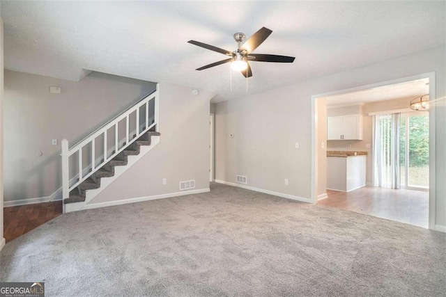 unfurnished living room featuring stairs, ceiling fan with notable chandelier, carpet flooring, and visible vents