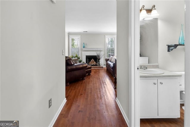 hall with dark wood-type flooring, a sink, and baseboards