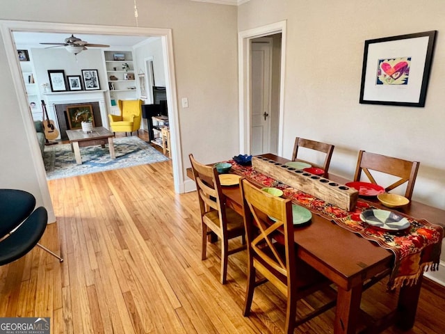 dining room with light wood-style flooring, a fireplace, a ceiling fan, built in features, and ornamental molding