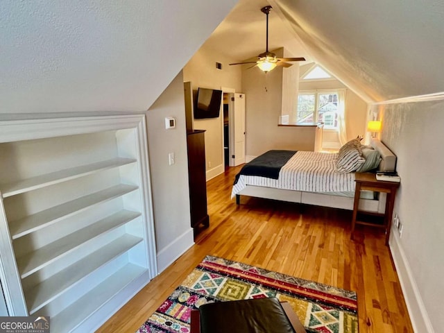 bedroom featuring lofted ceiling, a textured ceiling, baseboards, and wood finished floors