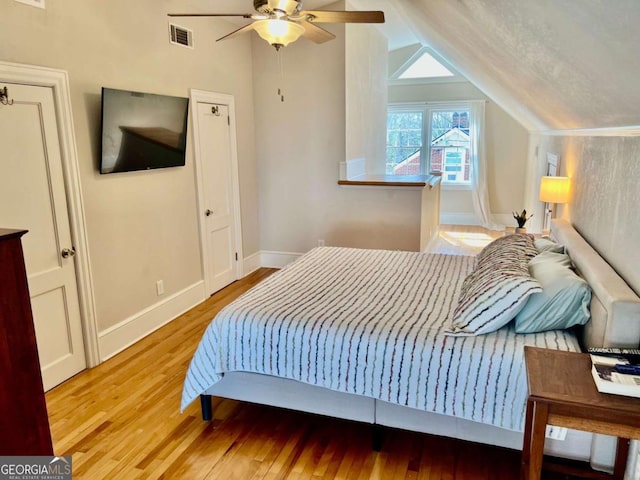 bedroom with lofted ceiling, wood finished floors, visible vents, and baseboards