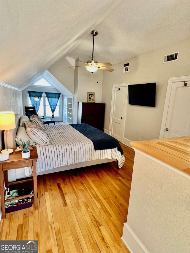 bedroom featuring visible vents, a ceiling fan, lofted ceiling, hardwood / wood-style flooring, and a textured ceiling