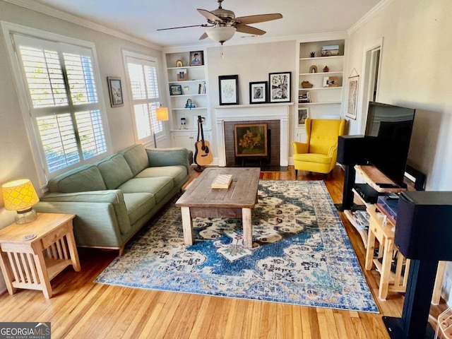 living area with built in features, a tile fireplace, crown molding, and wood finished floors