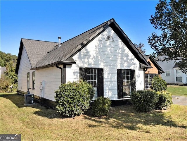 back of property featuring central AC unit, a lawn, and a shingled roof