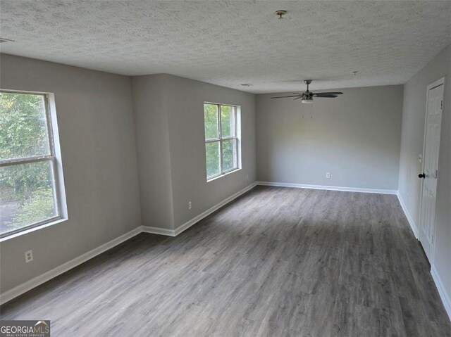 unfurnished room with a textured ceiling, plenty of natural light, wood finished floors, and baseboards