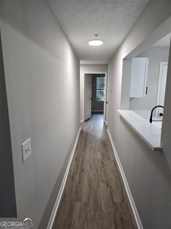 corridor featuring dark wood-type flooring, a sink, a textured ceiling, and baseboards