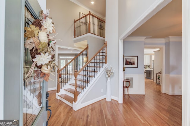 entryway with stairs, wood finished floors, a towering ceiling, and ornamental molding