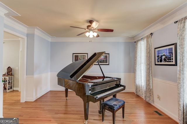 living area with light wood-type flooring, a wainscoted wall, visible vents, and ornamental molding