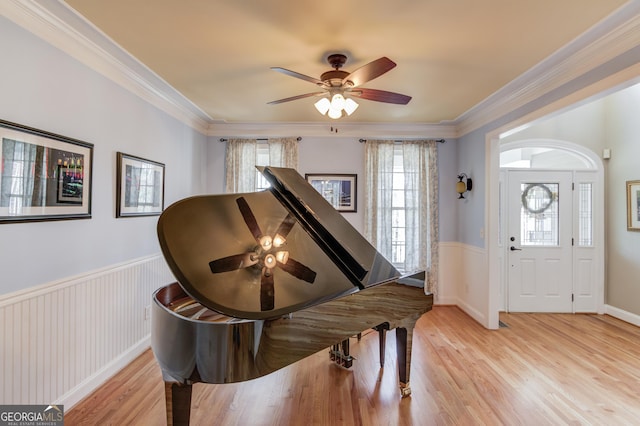 foyer featuring ceiling fan, crown molding, light wood-style floors, and wainscoting