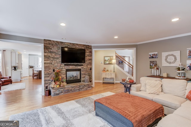 living room featuring light wood finished floors, a fireplace, stairs, and crown molding