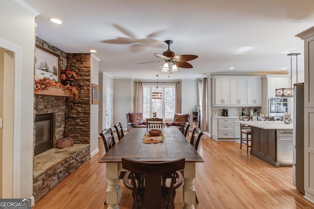 dining space with crown molding, a stone fireplace, recessed lighting, light wood-style flooring, and a ceiling fan